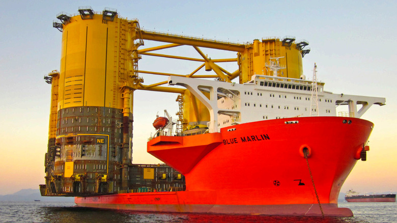 A ship called the Blue Marlin with an orange hull cruising on the ocean with an oil platform on top of it.