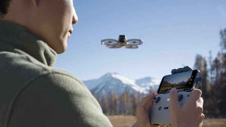 A person flying a DJI drone with a controller attached to a smartphone