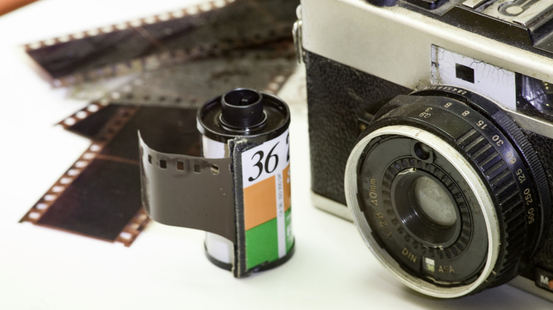Vintage 35mm film camera with film canister and developed negatives on white background.