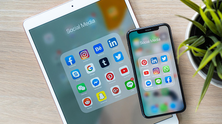 An iPhone sitting on top of an iPad on a wooden surface