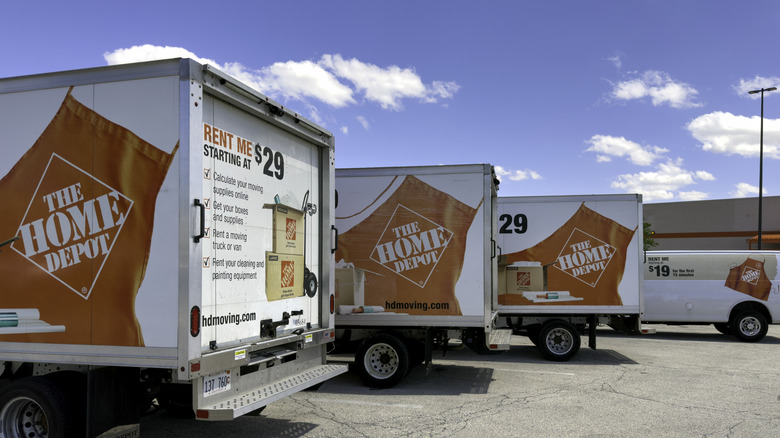 Several white Home Depot-branded delivery trucks in a parking lot in front.