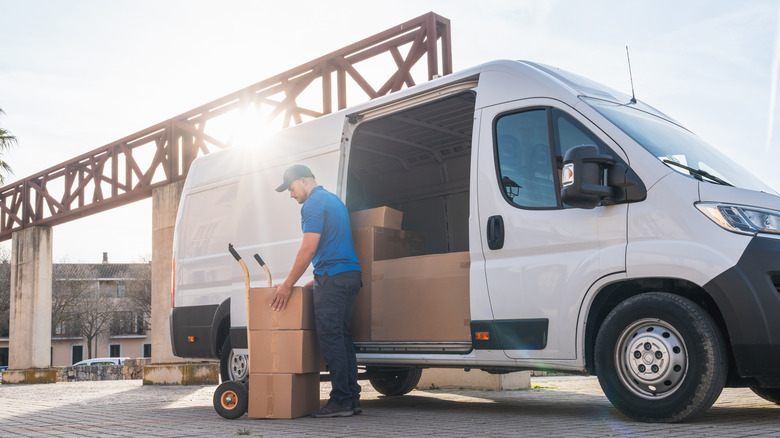 A delivery driver in uniform unloading a package stack from the open side door of a white delivery van.
