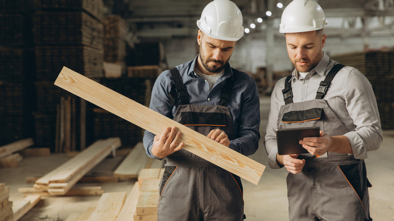 Two people holding cut wood in a large building.