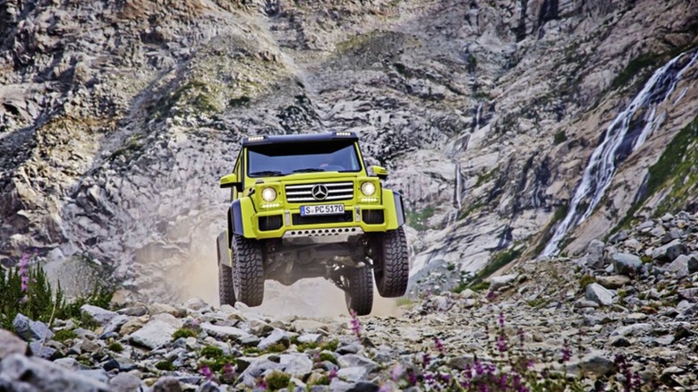 An electric green Mercedes-Benz G550 4x4² leaping over rocky terrain in a mountainous setting