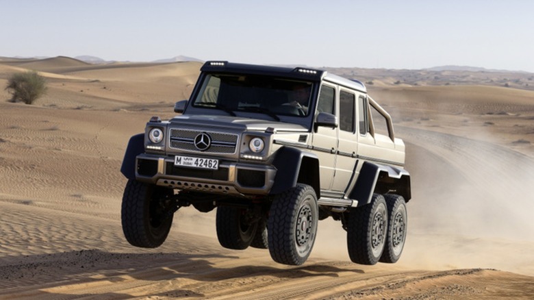 A Mercedes-Benz G63 AMG 6x6 soaring over a small sandy hill with all six tires in the air