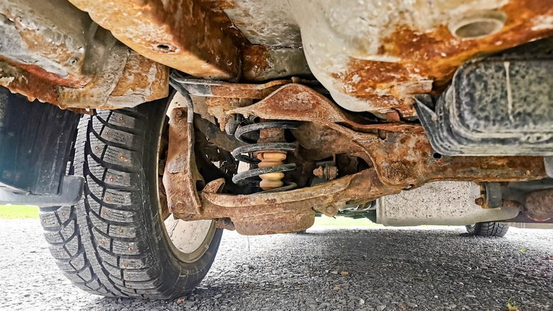 The exceptionally rusty undercarriage of a vehicle sitting on pavement