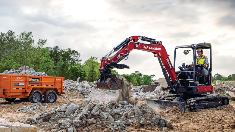 A man uses an excavator. A Home Depot rentable trailer can be seen nearby.