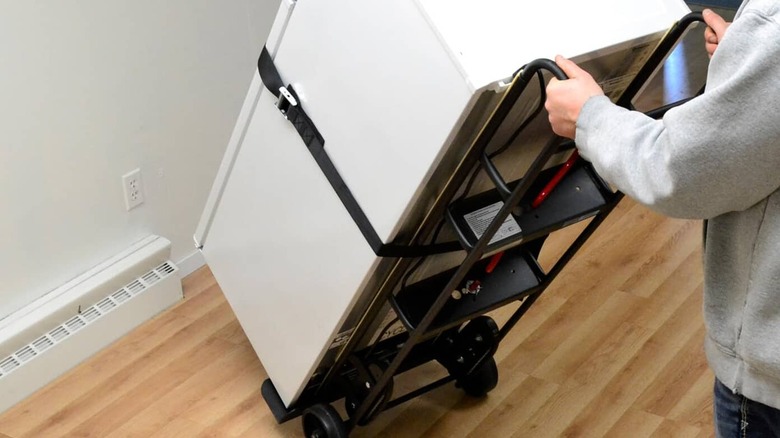 A person carries a fridge on an appliance dolly