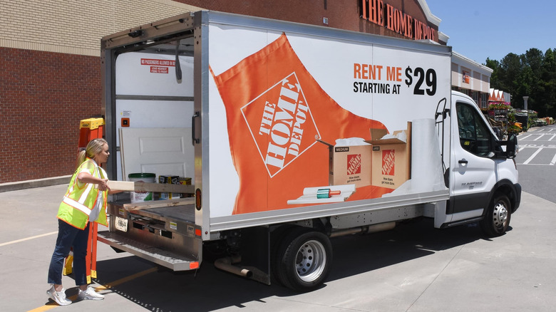 A woman loads wooden material into a Home Depot truck