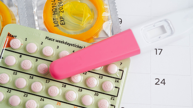 Condoms, birth control pills, and a pregnancy test on a white calendar.
