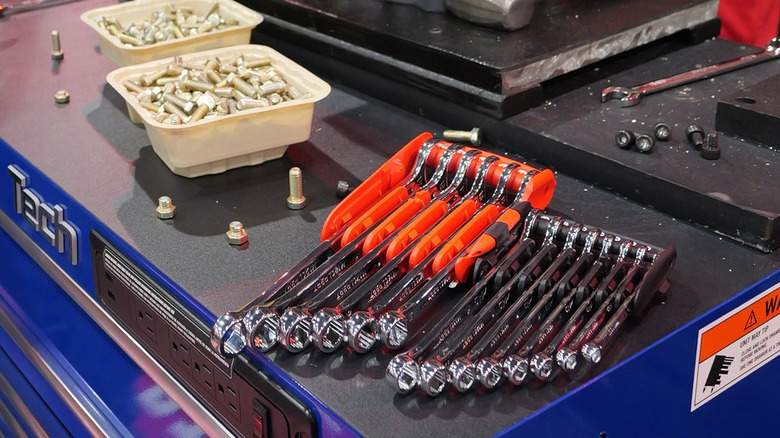 A blue Mac tools box with a box-end wrench set and some buckets of bolts sitting on top.