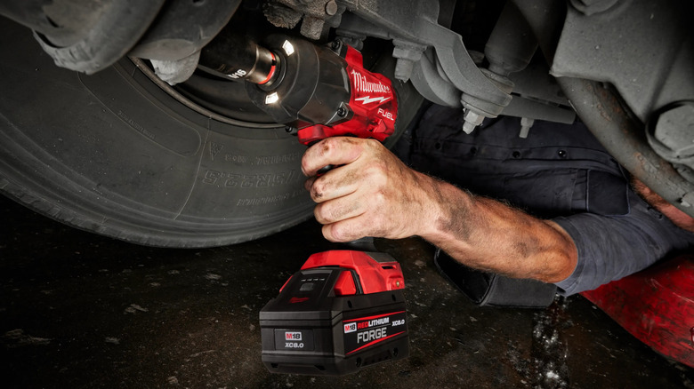 A partial view of an auto technician under a vehicle using an M18 Fuel impact to remove a bolt near a tire.