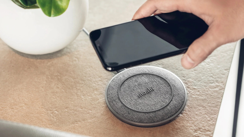 Hand holding an iPhone over the Mosi Otto Q Charging Pad.