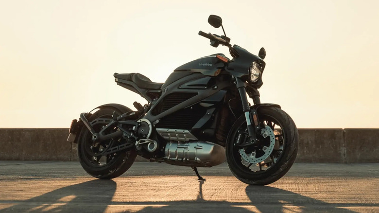 A black LiveWire electric motorcycle parked on a concrete surface at sunset, casting long shadows with a warm glow highlighting its sleek and modern design.