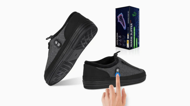 A pair of black Kamlif heated slippers near a box, a hand demonstrates where the buttons are on the shoes.