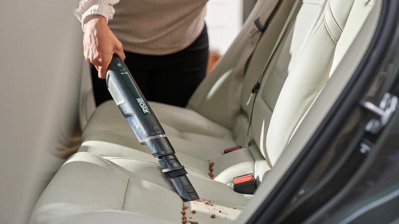 A person uses a Ryobi USB Lithium HP compact hand vacuum cleaner in a car.