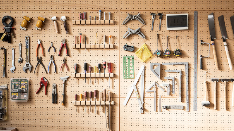 A frontal shot of a large brown tool rack on a wall with many tools on it.
