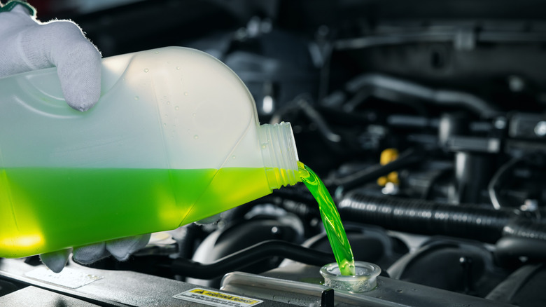 A person pouring a container of coolant into a radiator