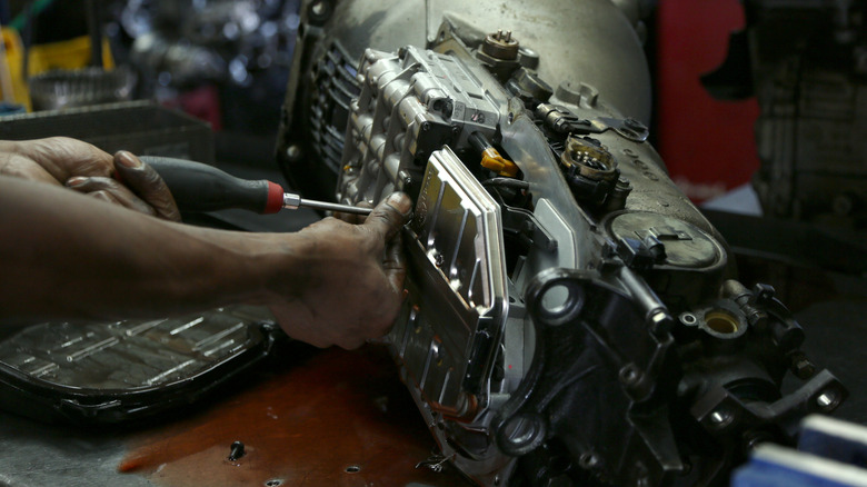 A person working on a car transmission with a screwdriver
