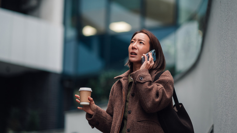 A person talking on the phone with a cup of coffee in their hand.