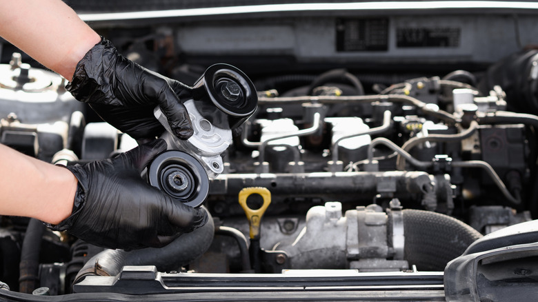 A man in work gloves holding a tensioner between a pulley and the serpentine belt