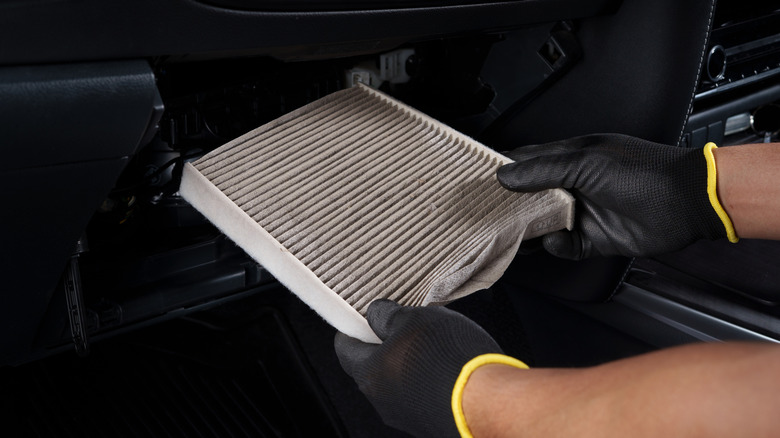 A mechanic in gloves installing a new cabin air filter into the glove box of a vehicle