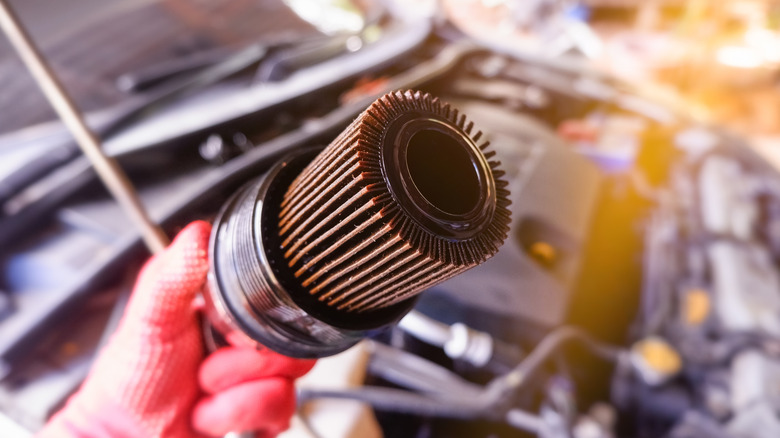 A technician holding a used, grubby car filter in front of the engine bay