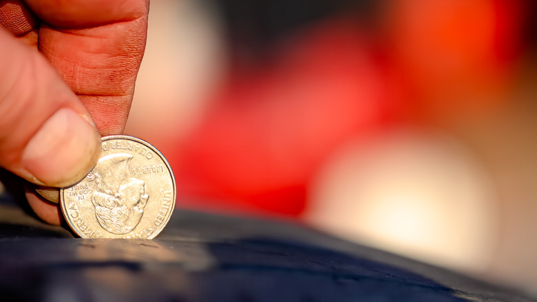 A person putting a quarter in upside down between the treads on a tire to test the depth