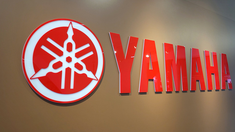 A Red and white Yamaha sign on a beige/ brown wall, illuminated
