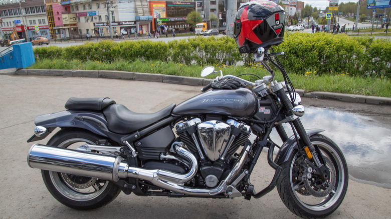amaha Road Star Warrior 1700 cruiser motorcycle parked on city pavement, featuring a V-twin engine, chrome exhaust, and a red Shark helmet mounted on the handlebars.