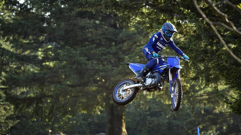 Motocross rider in Yamaha gear performing a jump on a Yamaha YZ85 dirt bike on an outdoor forest trail track.