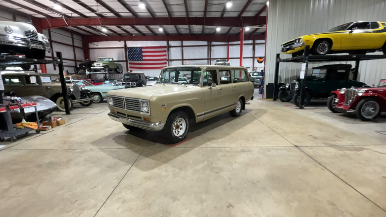 A beige International-Harvester Travelall SUV standing inside a car storage garage with other vintage cars in the background.