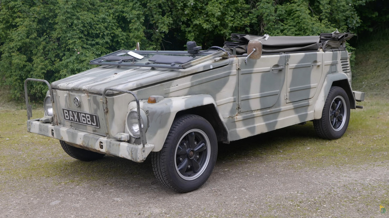 A grey and white camouflaged Volkswagen Type 181 utility vehicle standing next to some trees.