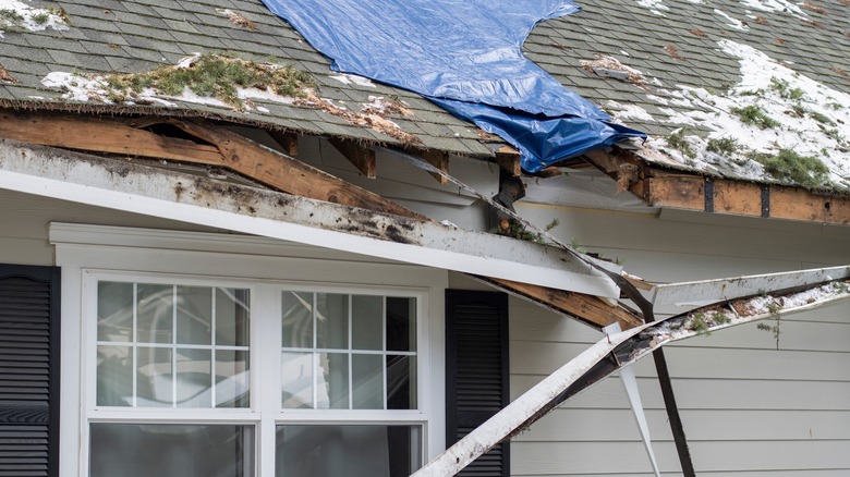 Roof with visible damage covered partially by a blue tarp