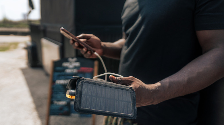 Man holding a portable solar power grid connected to a phone