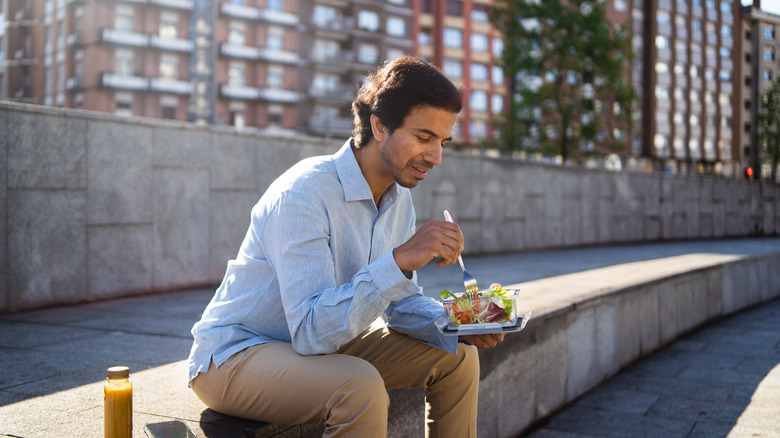 Man sitting on a brick wall eating a salad
