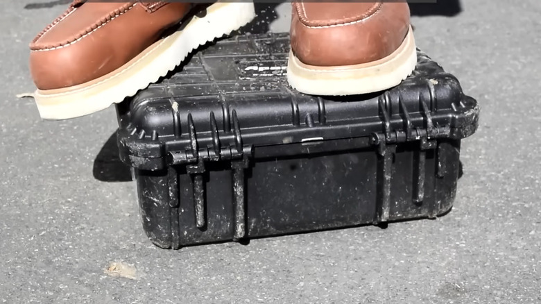 Brown shoes standing atop a black suitcase-style container