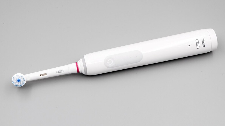 An Oral B electric toothbrush resting on the ground against a grey backdrop