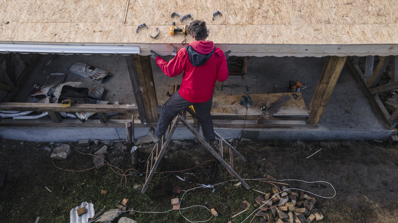 DIYer on a stepladder working on a complicated roof installation project