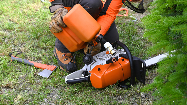 A person pouring gasoline into a chainsaw's fuel tank