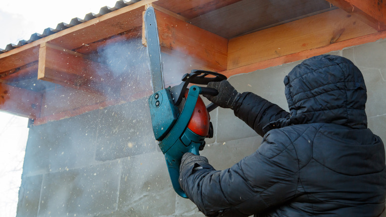 A person using a chainsaw to shave wood off a roof