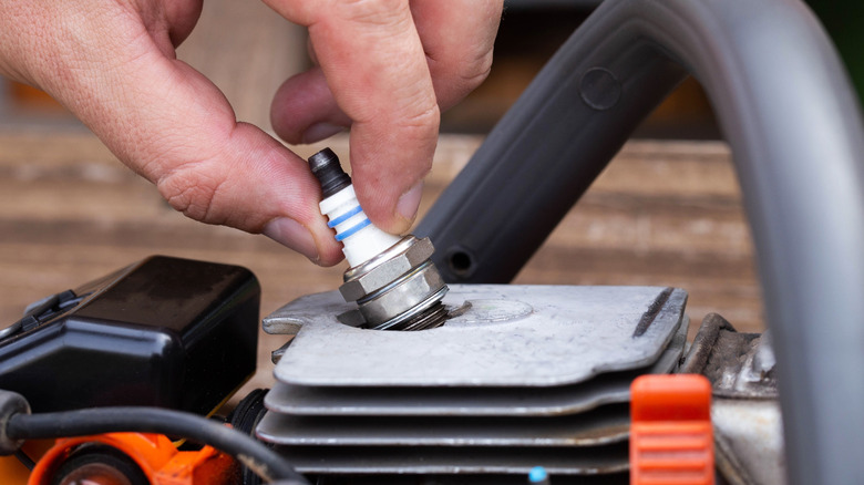 A hand pulling out a spark plug from a chainsaw's engine
