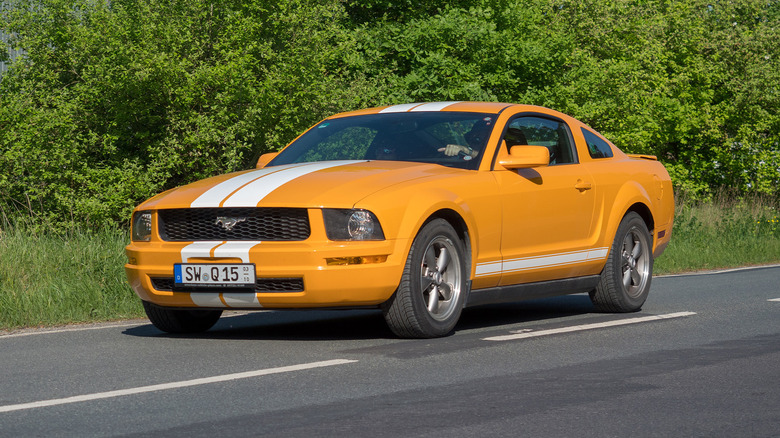 An orange Ford Mustang driving on a country road