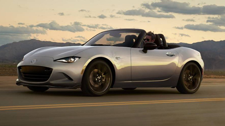 A man driving a Mazda Miata with the top down on a country road