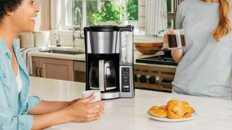 Ninja 12-cup drip coffee maker next to two women on a counter in a kitchen