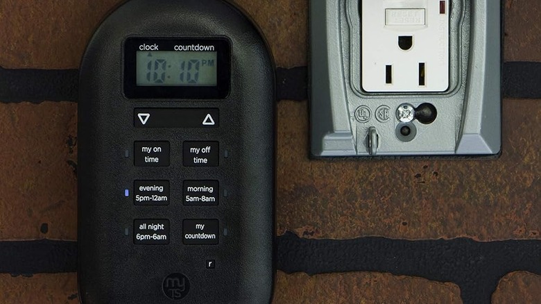 The digital outlet timer attached to the side of a brick wall next to an outlet