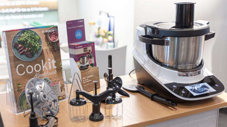 A Bosch Cookit setup with its various attachments and a cookbook displayed on a table.