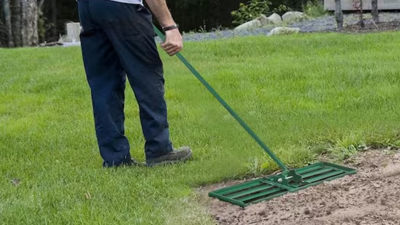 A worker spreading soil with lawn leveling rake