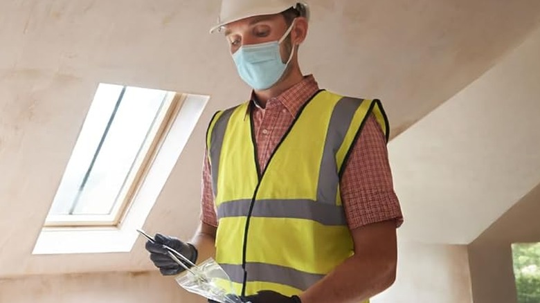 A man in a highlight vest and a mask putting something in a bag.
