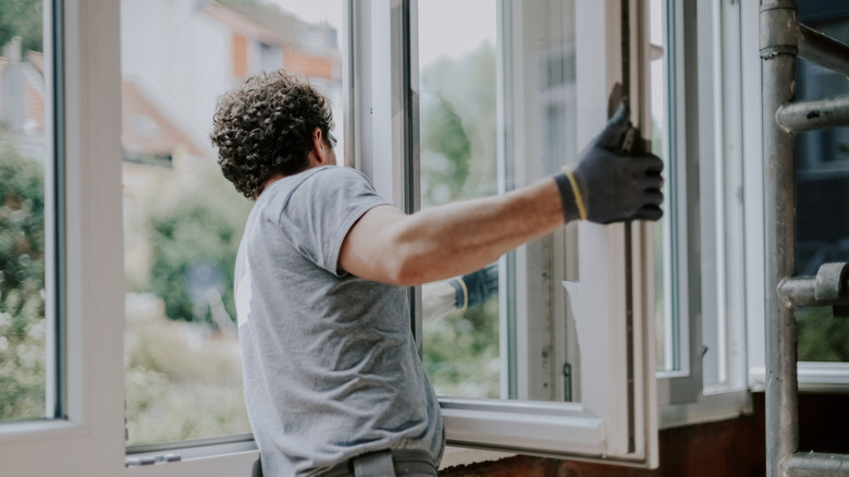 One young person in a gray uniform stands from the back and repairs installing a window frame in a house.